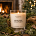Alpine Light soy candle by Soulful Sage glowing beside evergreen branches and a warm fireplace, with fresh evergreen, cedar, and fir notes.