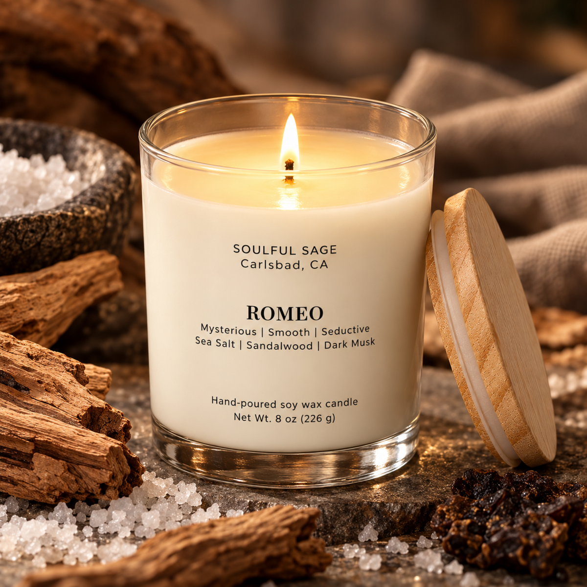 Romeo soy candle burning with a visible melt pool and wick, surrounded by sea salt, sandalwood, and dark wood accents.
